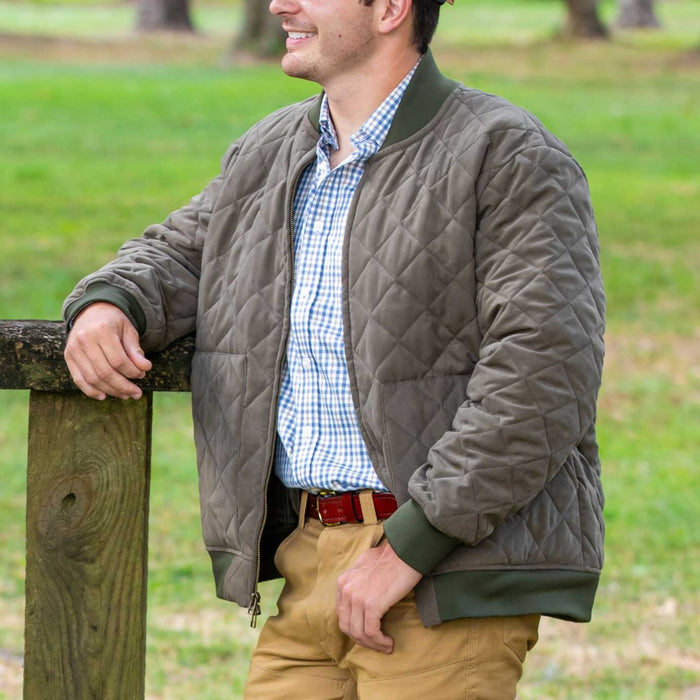 Man wearing an olive green quilted bomber coat with a brushed matte finish and ribbed trim over a plaid shirt.