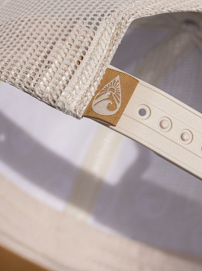 Close-up of the adjustable snapback strap and gold Waihana brand label on a cream white mesh trucker hat.
