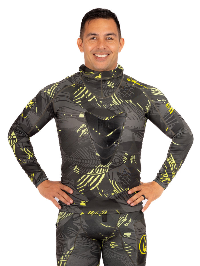 Male model wearing the Waihana Lime Fishbone Hooded Spearfishing Rashguard with matching pants, featuring a dark grey and yellow-green fish-scale camouflage print, hands on hips, smiling against a white background.