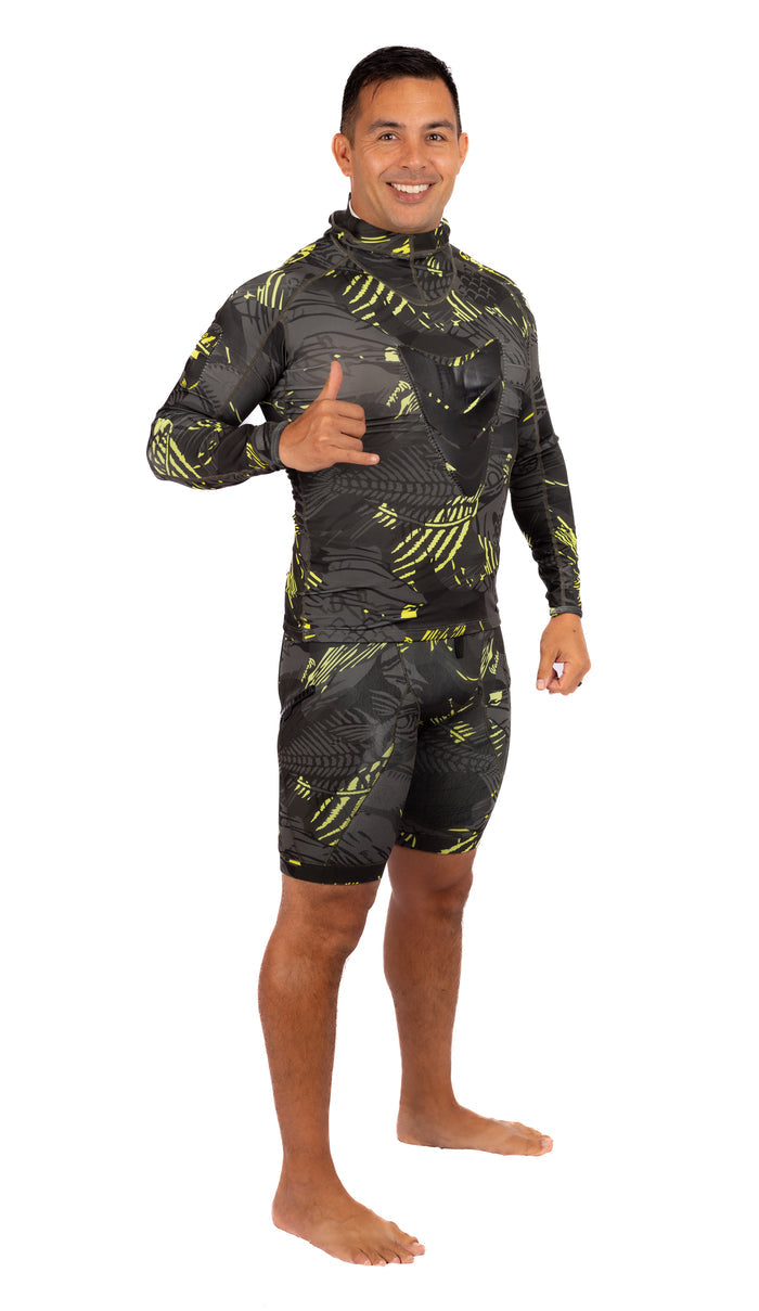 Male model smiling and giving a shaka sign while wearing the Waihana Lime Fishbone Hooded Spearfishing Rashguard top and matching shorts in a dark camo pattern with yellow-green fishbone print.