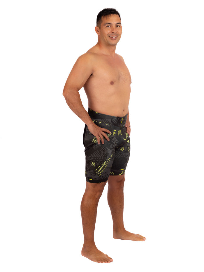 Male model wearing Waihana Lime Fishbone Tech Jammers, dark swim shorts with bold yellow-green fishbone graphic print, shown from a three-quarter side angle against a white background.