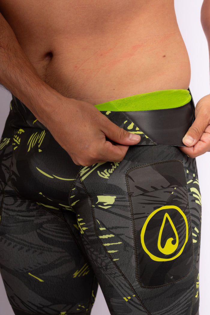 Close-up of a male model pulling back the neoprene waistband of Waihana Lime Fishbone Tech Jammers, revealing a bright lime green interior lining, with the Waihana drop logo visible on the thigh.