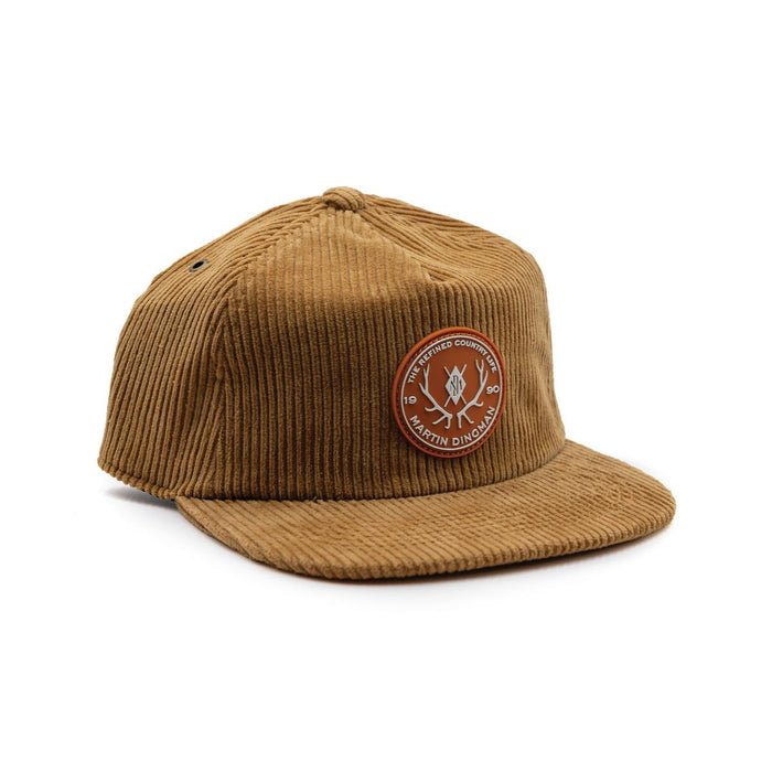 Tan six-wale cotton corduroy country cap with a circular leather logo patch and adjustable brass slide.