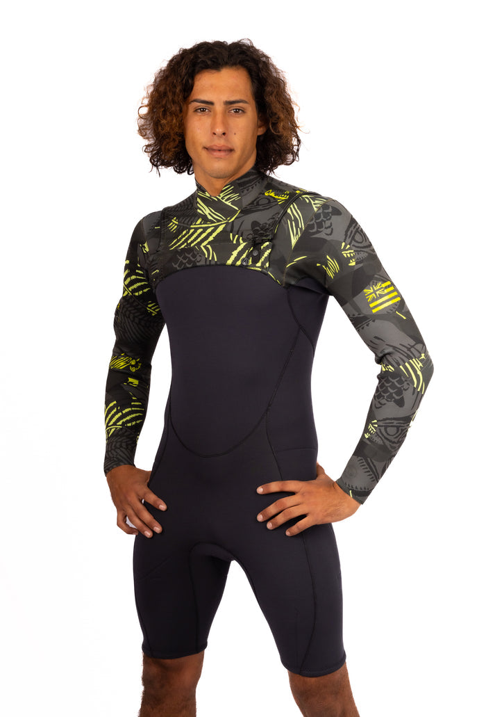 Male model wearing the Waihana Men's Lime Fishbone Long Sleeve Spring Suit, a black neoprene surf spring suit with bold lime yellow fishbone and Hawaiian-print panels on the chest and long sleeves, standing against a white background.
