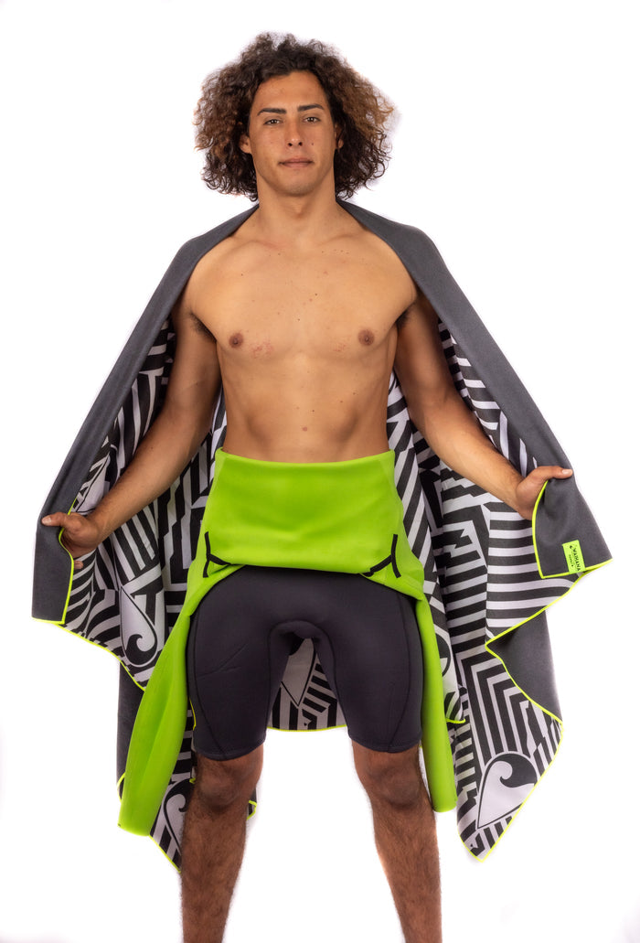 Male model displaying a Waihana black-and-white tribal-print towel with neon yellow edging while wearing lime green and dark grey wetsuit pants in a studio setting.