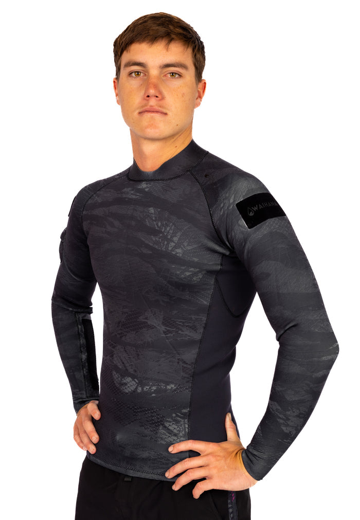 Male model wearing the Waihana Men's Tropicam Black rear-zip neoprene surf rashguard top featuring a dark grey camouflage print and Waihana logo patch on the left sleeve.