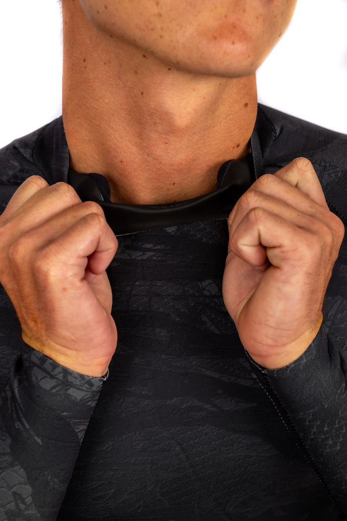 Man pulling open the neckline of the Waihana Men's Tropicam Black rear-zip surf rashguard, highlighting the collar and textured black camo fabric.