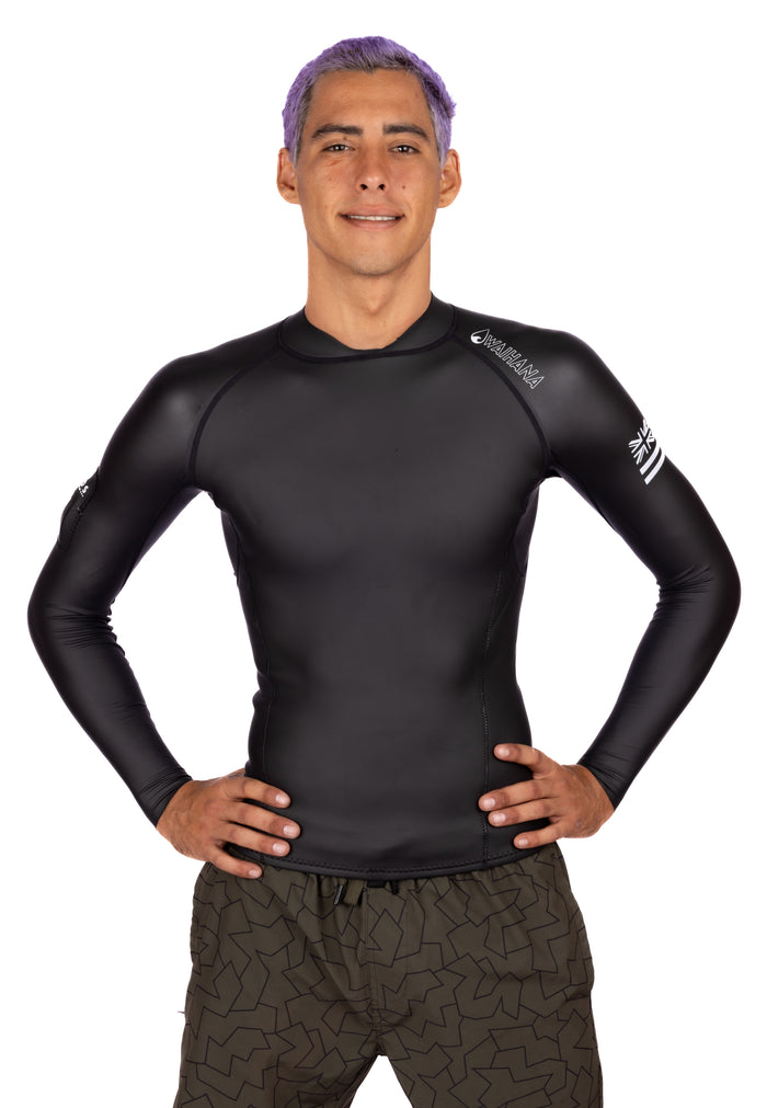 Male model with purple hair wearing a black long-sleeve Waihana WAI-FLEX men's surf impact top with Hawaiian flag logo on the sleeve, paired with olive board shorts, against a white studio background.