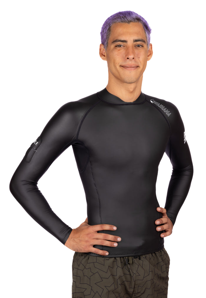 Male model with purple hair wearing a black Waihana Men's WAI-FLEX long-sleeve surf top impact suit, standing with hands on hips against a white background.