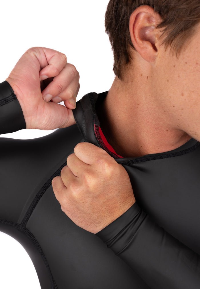 Man pulling open the neck collar of a black WAI-FLEX impact surf top, showing the red interior lining and neoprene construction at the seam.