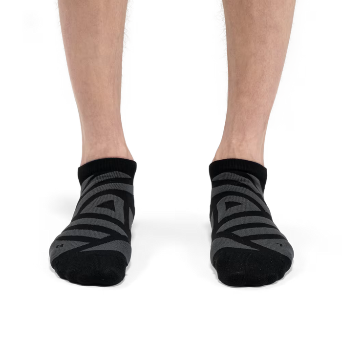 Black and grey On Running performance low socks with technical mesh paneling worn on feet against a white background.