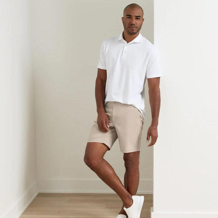 Man wearing beige Peter Millar Crown Comfort stretch shorts with an 8-inch inseam and a white polo shirt.