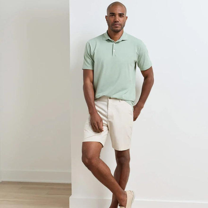 Man wearing beige Peter Millar Crown Comfort 8-inch inseam shorts with a light green polo shirt.