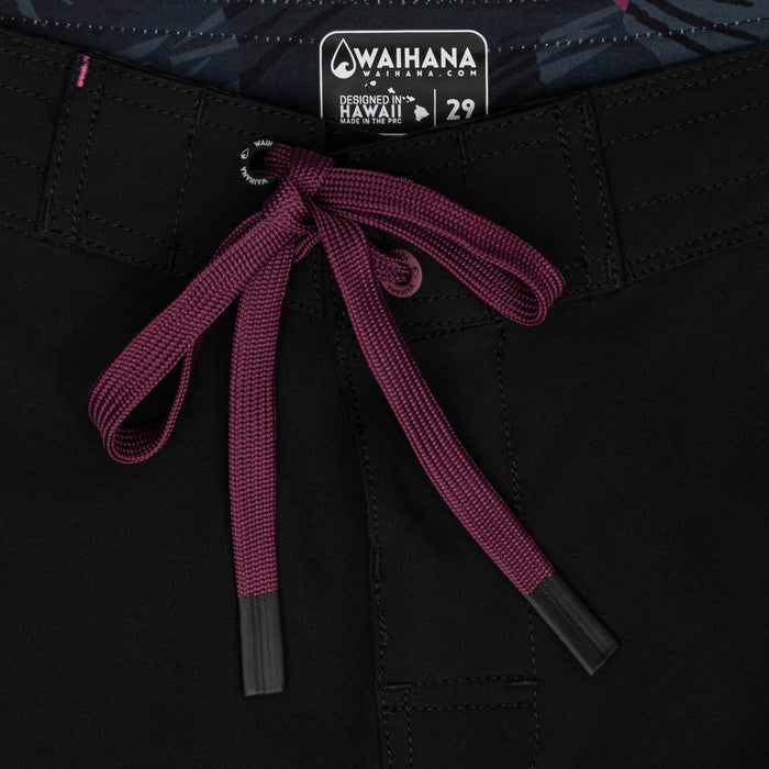 Close-up of the waistband of Waihana Pink Fishbone W1 board shorts in black, featuring a burgundy drawstring tie, Waihana branded grommet, and 'Designed in Hawaii' label showing size 29.