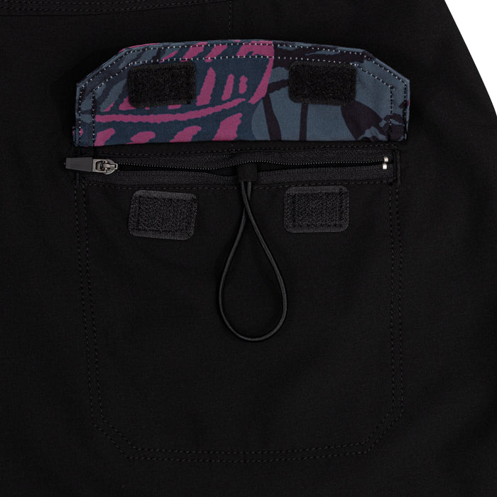 Close-up of the zippered cargo pocket and Pink Fishbone camo waistband on the Waihana W1 Board Shorts, featuring velcro tabs and a rubber zipper pull loop on black neoprene-style fabric.