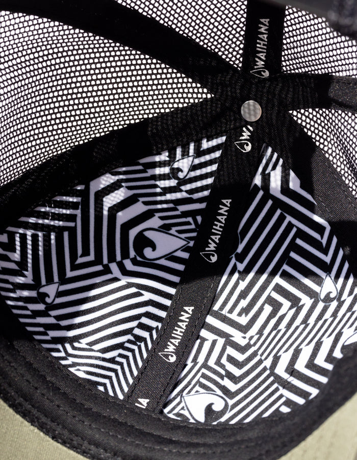 Interior close-up of the Waihana Ranger Green Mauka Trucker hat revealing a bold black and white geometric tribal-print lining with Waihana branding on each panel and seam tape.