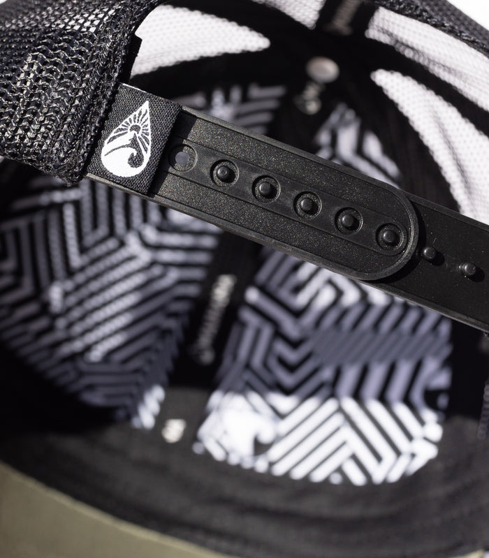 Close-up of the interior of the Waihana Ranger Green Mauka Trucker hat, highlighting the black snapback adjuster with Waihana logo patch and bold geometric black-and-white lining pattern.