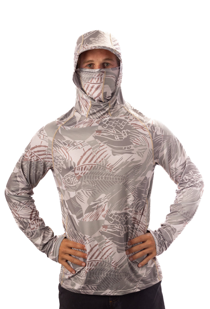 Male model wearing the Waihana Sandy Sun Shirt in Sandy Fishbone camo print with integrated hood and face gaiter pulled up, hands on hips, against a white studio background.