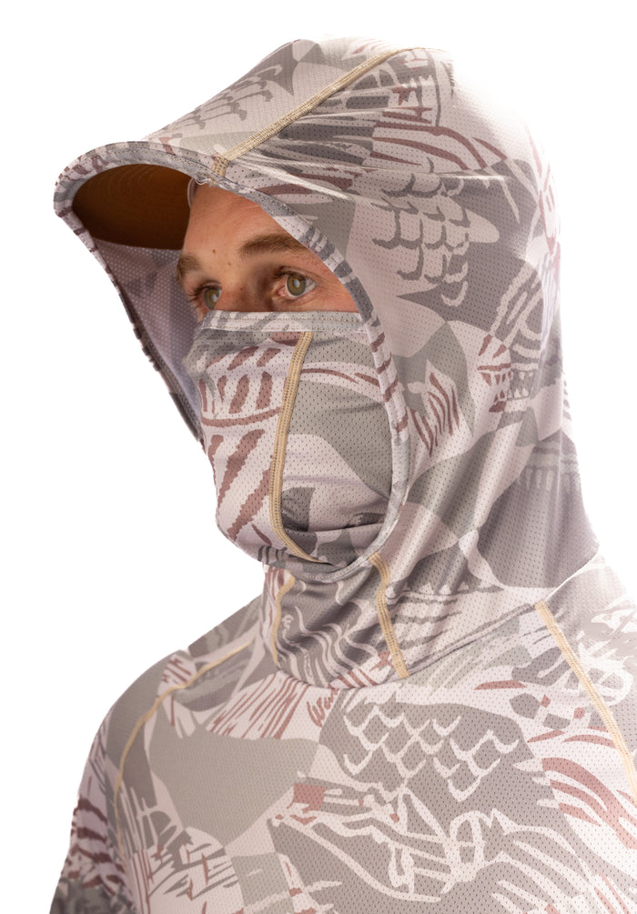 Male model wearing the Waihana Sandy Sun Shirt in Sandy Fishbone camo pattern with the integrated hood up and face mask pulled over his nose, showing full sun protection coverage.