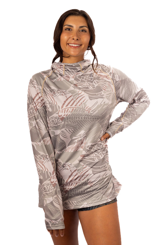 Woman modeling the Waihana Sandy Sun Shirt in Sandy Fishbone print, a long-sleeve hooded sun shirt featuring an all-over fish skeleton pattern in grey and dusty rose tones.