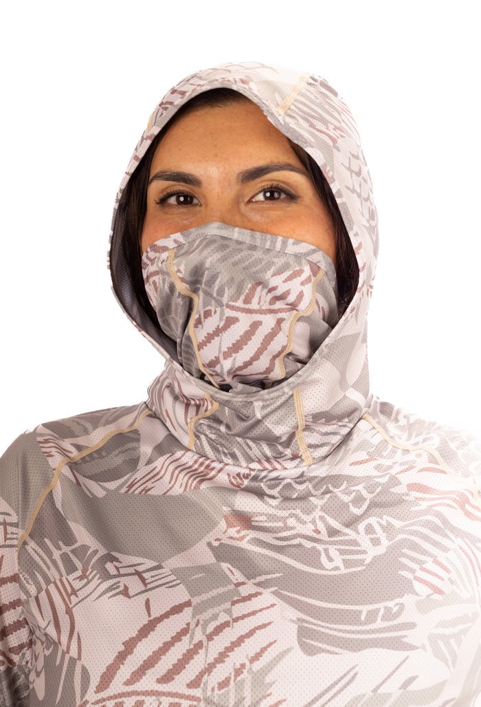 Woman wearing the Waihana Sandy Sun Shirt in Sandy Fishbone print with the hood up and built-in face mask covering her nose and mouth, shown against a white background.