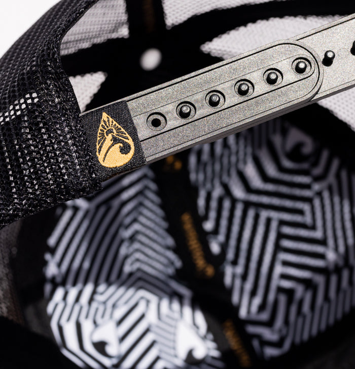Close-up of the interior back panel of the Waihana Sunset Beach Trucker hat, highlighting the silver snapback adjuster, black mesh sides, gold Waihana logo label, and black-and-white geometric swirl lining.