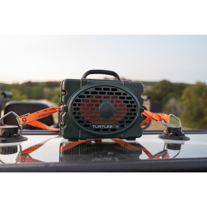 Green Turtlebox speaker secured to a flat surface with bright orange 41-inch durable tie-down straps.