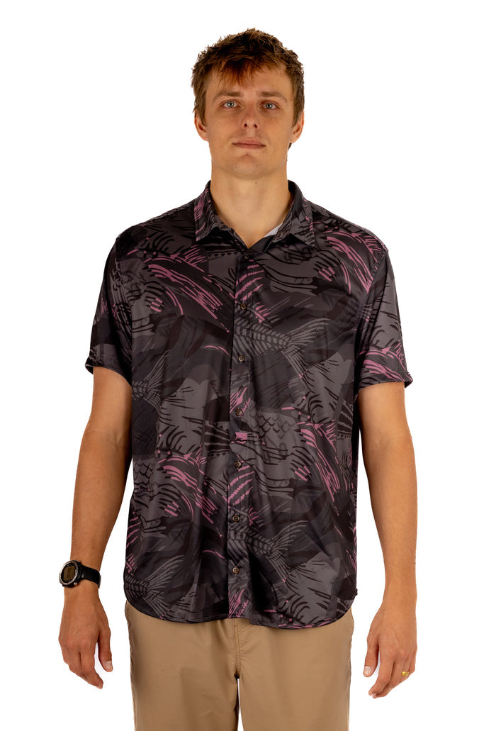 Male model wearing the Waihana Unisex Pink Fishbone Aloha shirt featuring a dark charcoal and pink tropical fish-bone print, paired with khaki shorts, photographed against a white studio background.