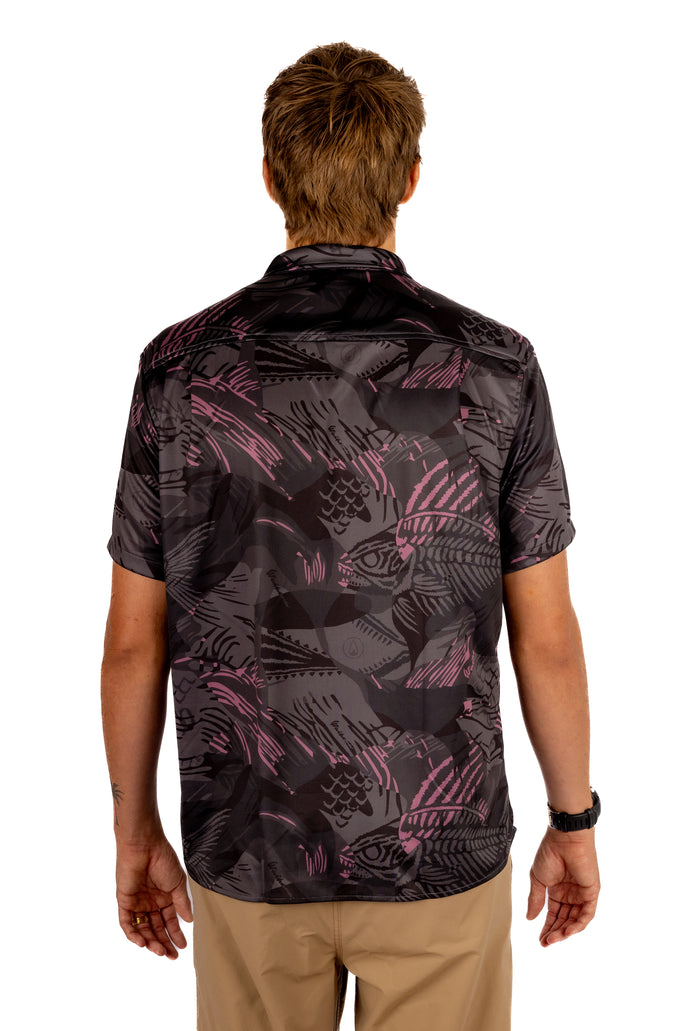 Man wearing the Waihana Unisex Pink Fishbone Aloha Shirt from behind, showcasing the dark short-sleeve button-up shirt with an allover pink bonefish skeleton print.