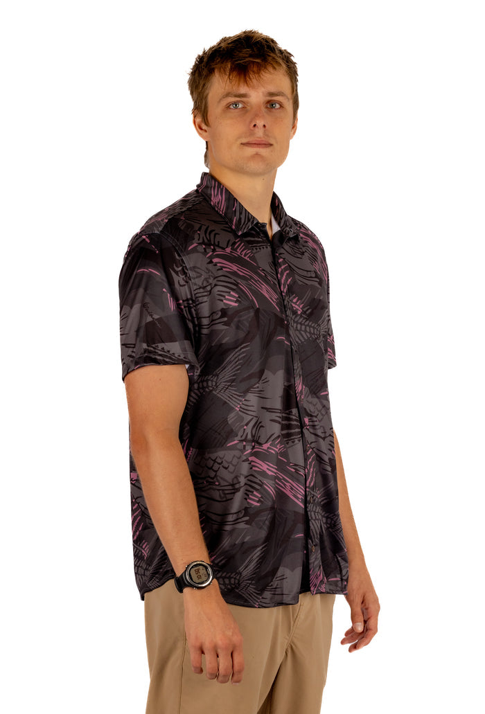 Male model wearing the Waihana Unisex Pink Fishbone Aloha Shirt in a dark charcoal and pink bonefish print, shown from a three-quarter side angle against a white background.