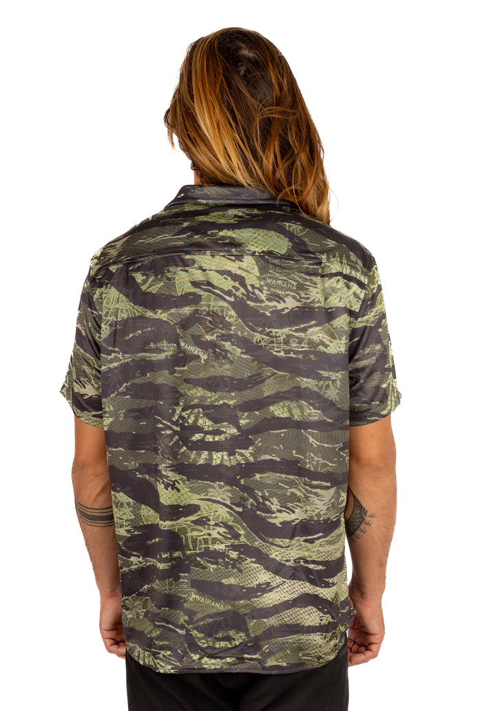 Back view of a long-haired male model wearing the Waihana Unisex Tropicam Aloha Shirt in Tropicam Green camouflage pattern, showing the short sleeves and button-up collar design.