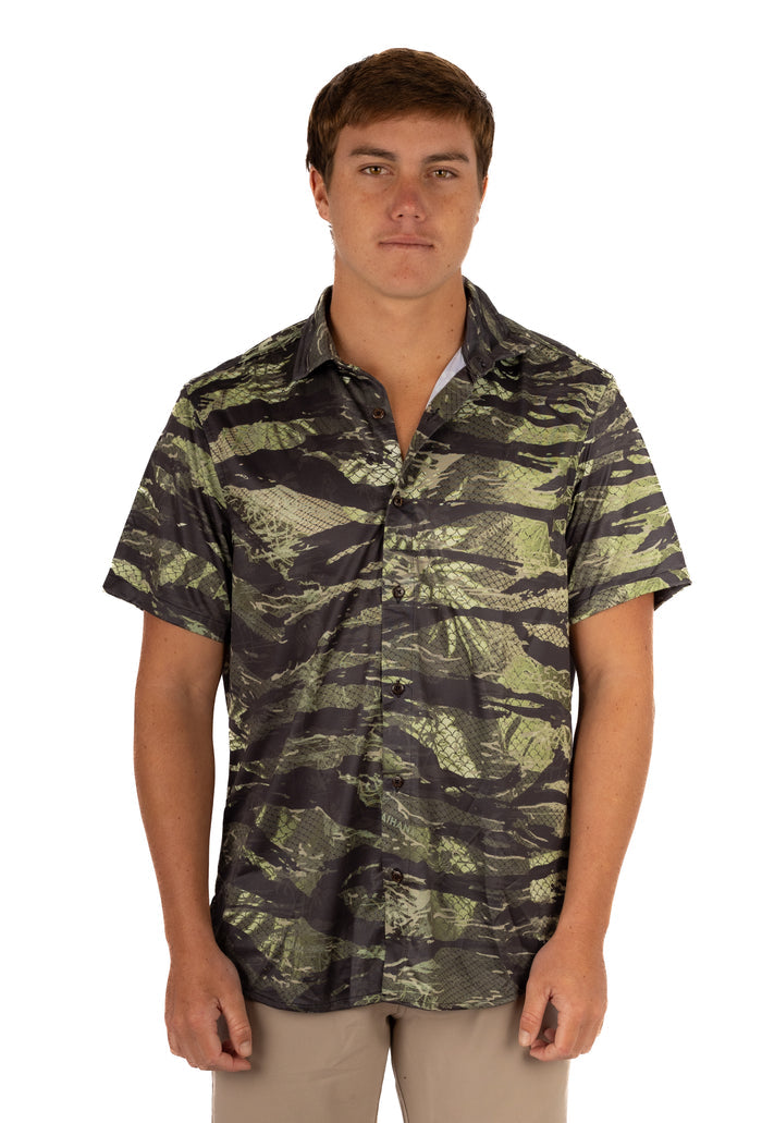 Male model wearing the Waihana Unisex Tropicam Aloha Shirt in Tropicam Green camouflage print, a short-sleeve button-up shirt with fish-scale texture overlay, shown from the front against a white studio background.