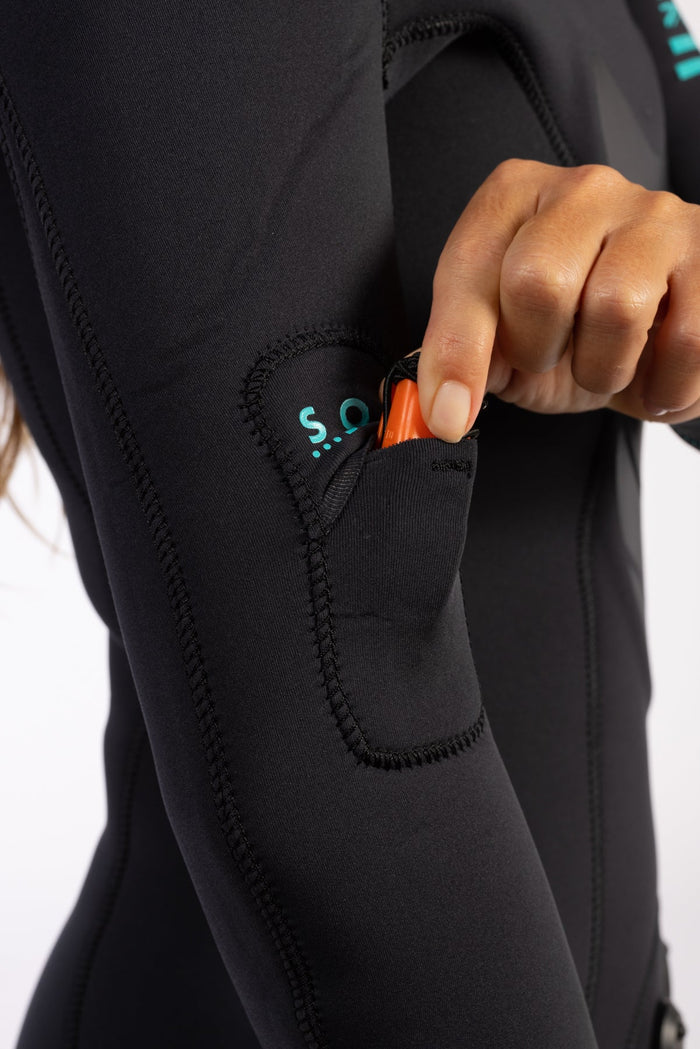 Close-up of a black Waihana Women's Essentials wetsuit thigh pocket with teal S.O.S. branding, with a hand retrieving an orange safety tool from the neoprene pocket.