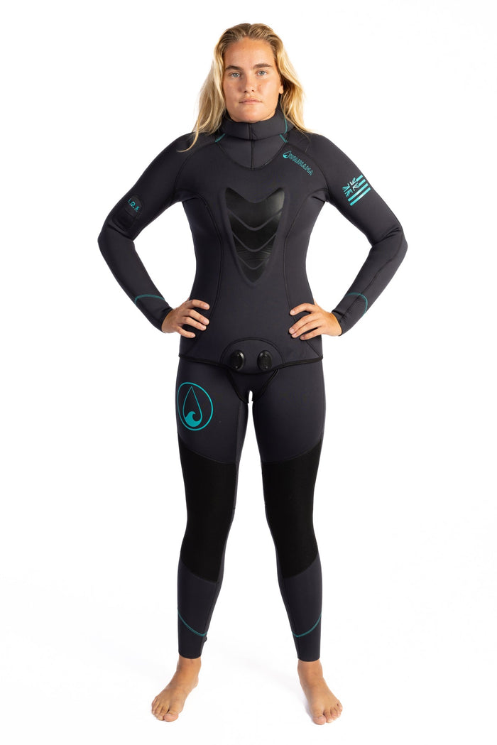Woman wearing a black Waihana Women's Essentials full-length wetsuit with teal stitching accents, chest loading pad, and Waihana branding, standing against a white studio background.