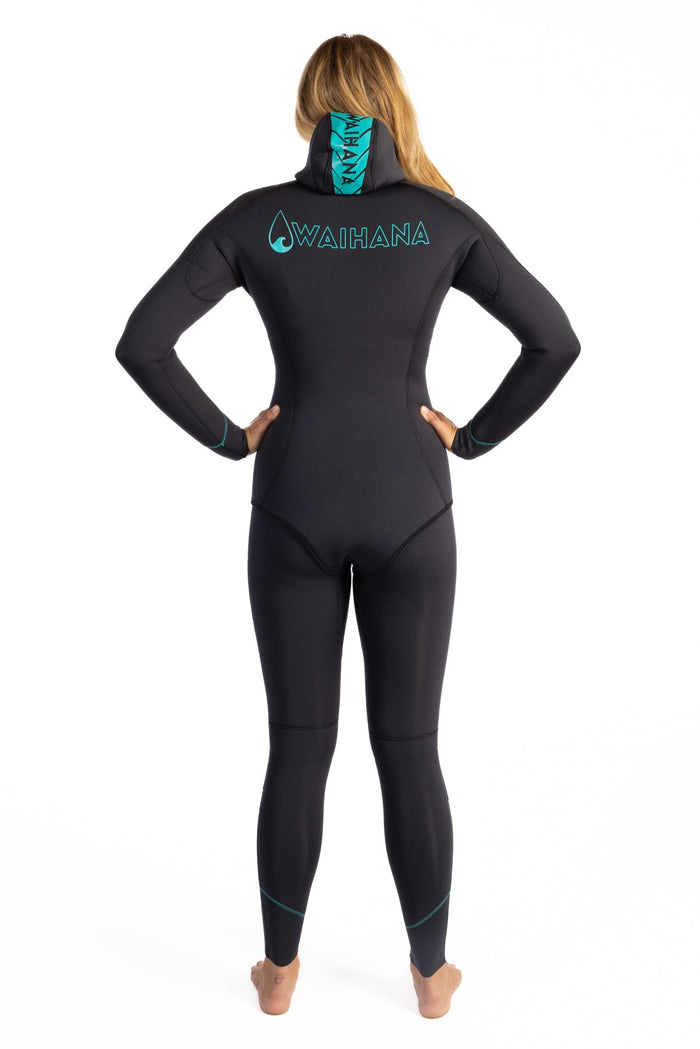 Back view of a woman modeling the Waihana Women's Essentials full-length black wetsuit with teal logo print and integrated hood, on a white studio background.